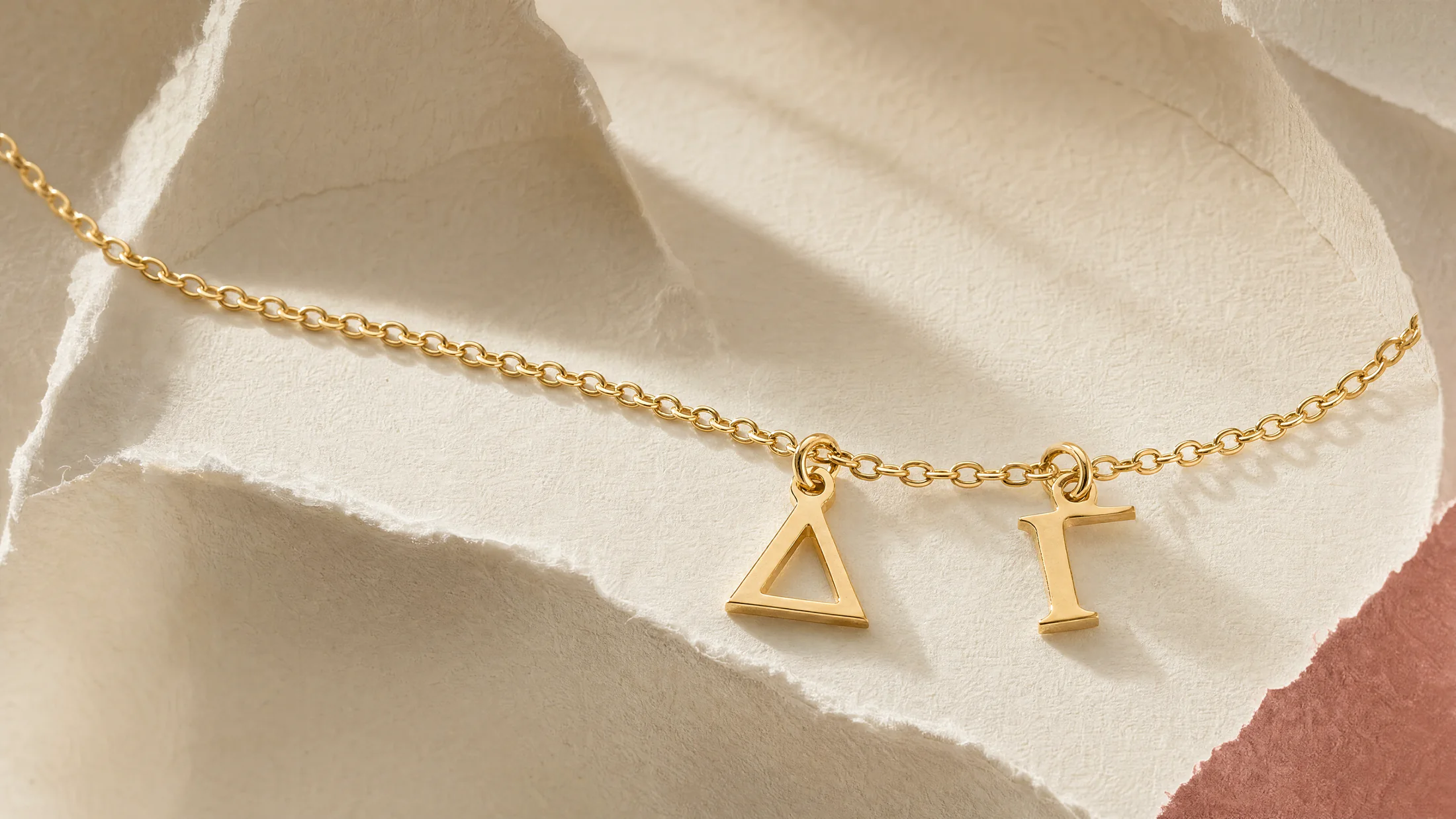 Delta Gamma gold letter pendants strung on a chain across sculpted cream paper