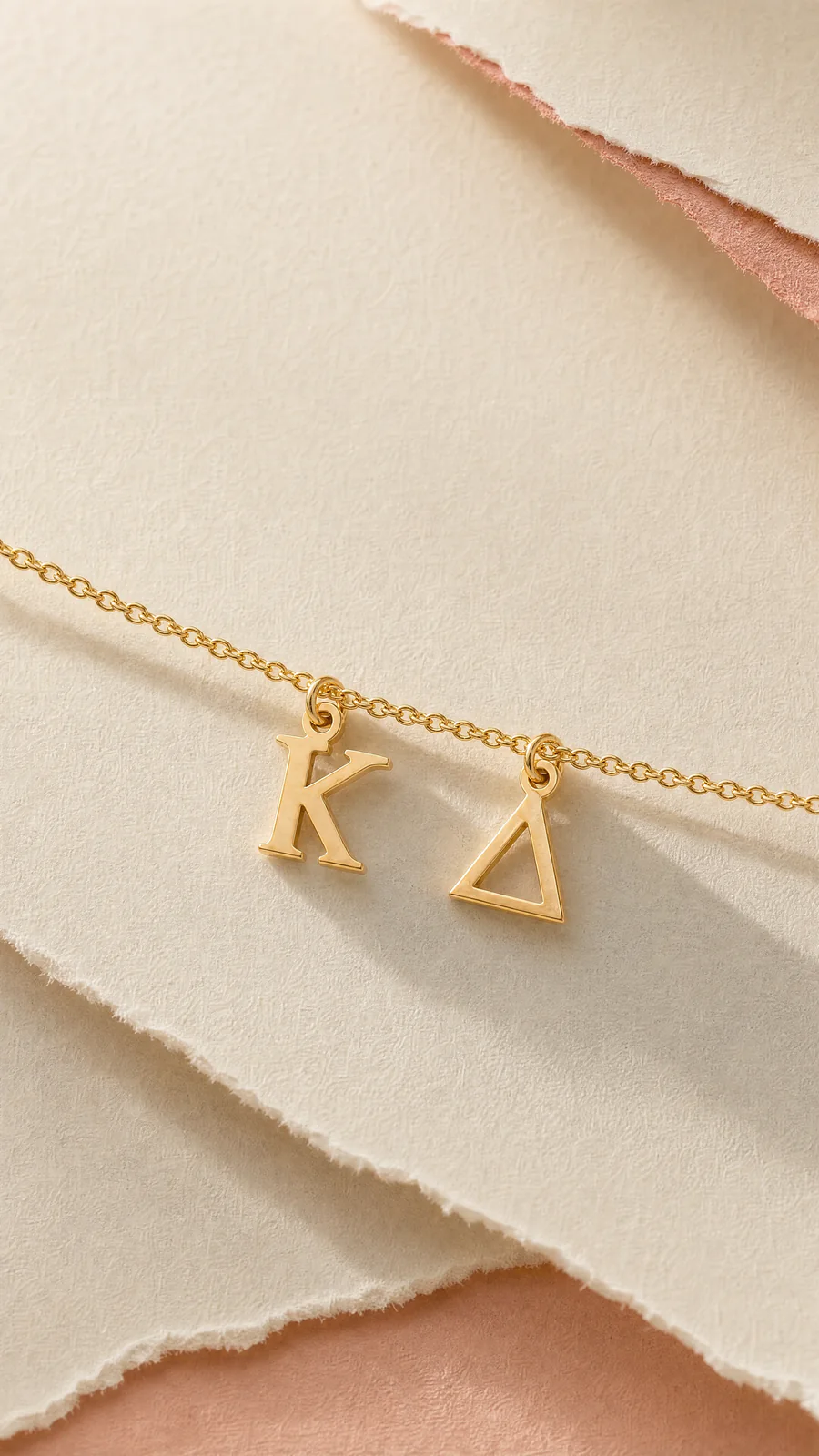 Kappa Delta gold letter pendants photographed on softly lit cream paper