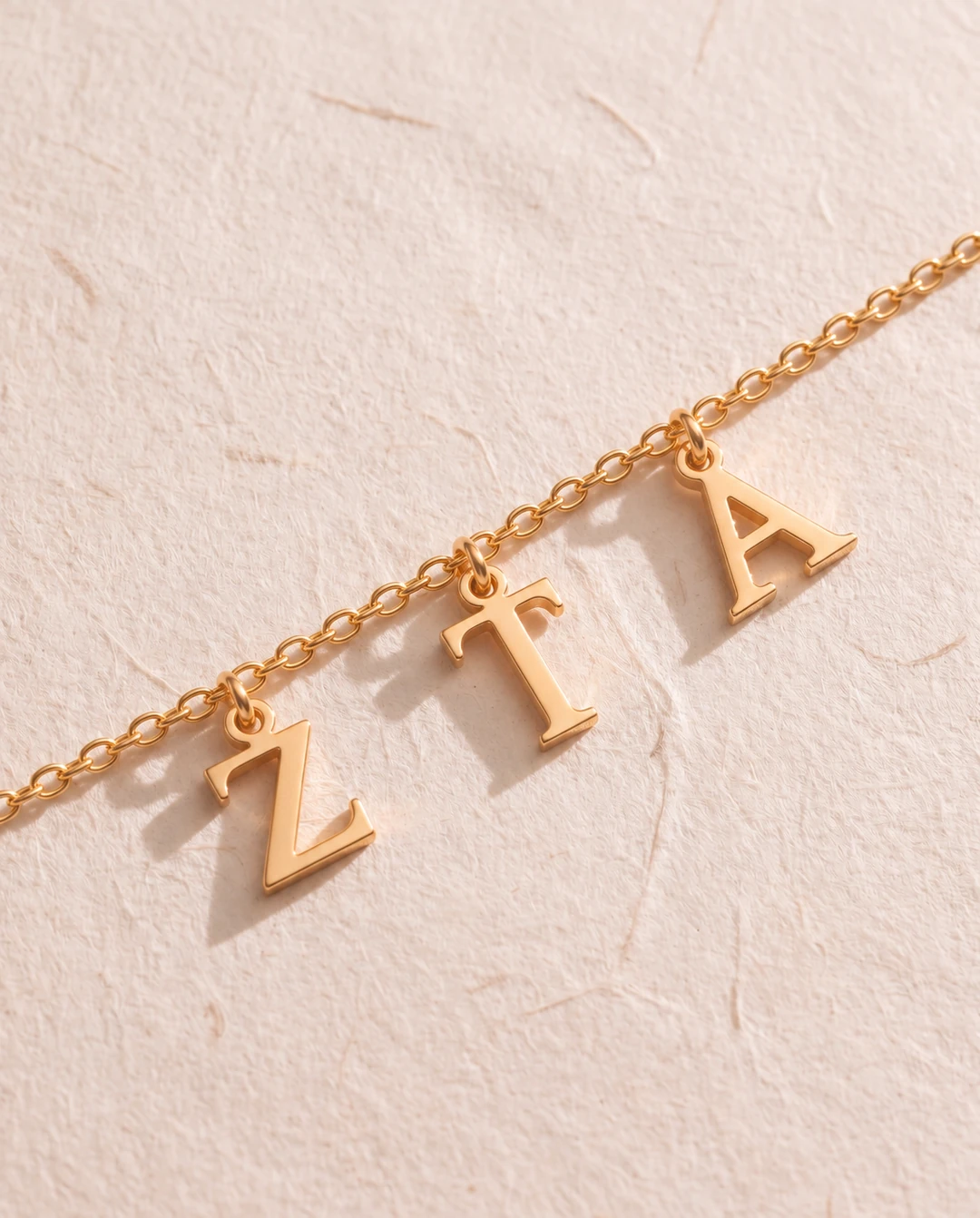 Zeta Tau Alpha gold letter pendants on textured blush paper